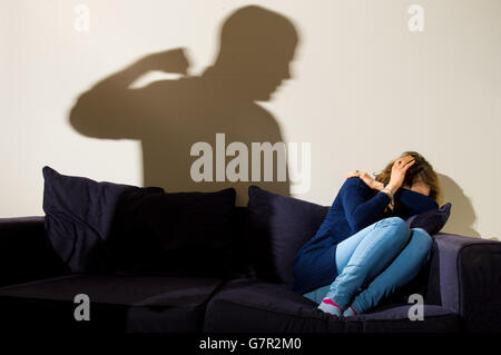 A shadow of a man with a clenched fist as a woman cowers in the corner. Stock Photo