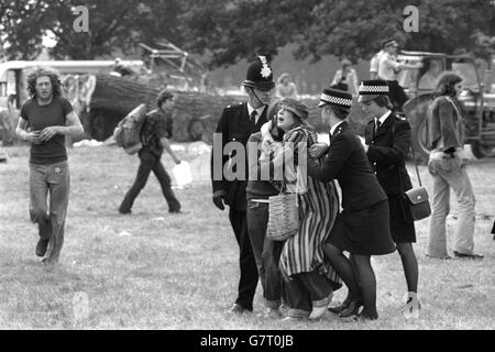 With two persuasive policewomen to help their departure, a girl and a man cling to each other as they leave the site of the Windsor Great Park Free Pop Festival. More than 600 police had swooped to break up the free pop festival. Stock Photo