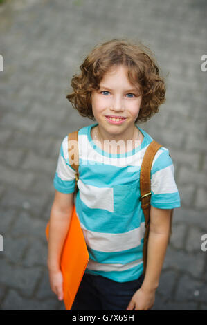 The schoolkid stand on a schoolyard and smiles. The boy has a nice face, a fair hair, an open look. It has behind shoulders a sa Stock Photo