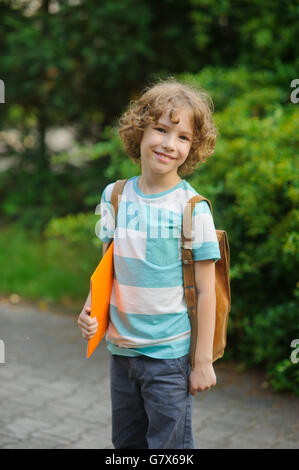 The pupil of elementary school stand on a schoolyard and smiles. The boy has a nice face, a fair hair, an open look. It has behi Stock Photo
