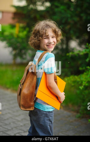 The pupil of elementary school on a schoolyard. The school student costs in a half-turn to the camera and smiles. Behind shoulde Stock Photo