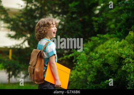 The schoolboy on a schoolyard. The school student stand in a half-turn to the camera. He looks in a distance and smiles. Behind Stock Photo