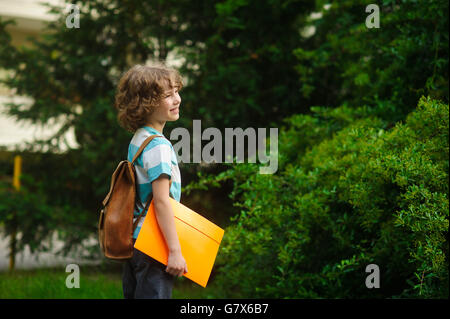 The first grader on a schoolyard. The school student stand in a half-turn to the camera. He looks in a distance and smiles. Agai Stock Photo