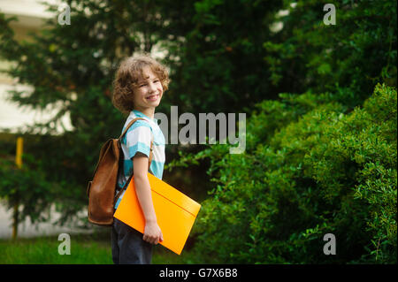 The pupil of elementary school on a schoolyard. The school student stand in a half-turn to the camera and smiles. Behind shoulde Stock Photo
