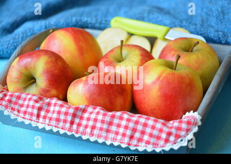 close up of red, yellow ,green apples in wooden bowl with knife and apple slices red white nostalgic countryside checkered doily Stock Photo