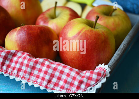 close up of red, yellow ,green apples in wooden bowl with knife and apple slices red white nostalgic countryside checkered doily Stock Photo