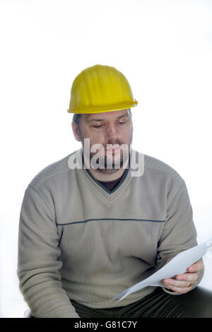 Young construction engineer wearing a yellow helmet reads a construction plan printed on paper Stock Photo