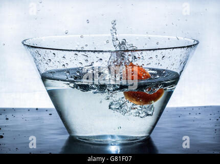 Orange splashes water in a big bowl on a black table Stock Photo