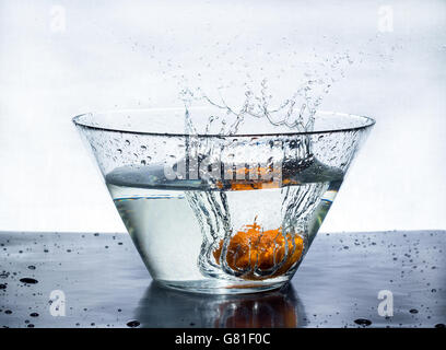 Orange splashes water in a big bowl on a black table Stock Photo