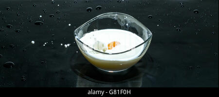 Fruits splashing milk in a round bowl on a black background Stock Photo