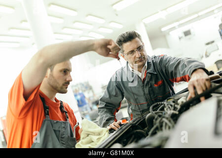 Car mechanics fixing car in garage - teamwork Stock Photo