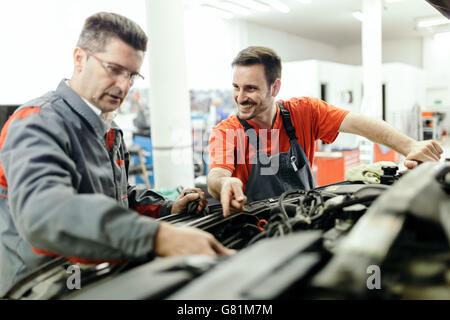 Car mechanics fixing car in garage - teamwork Stock Photo