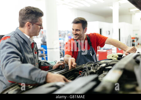 Car mechanics fixing car in garage - teamwork Stock Photo