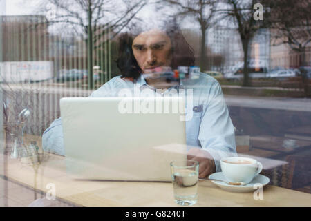 Man using laptop and having coffee seen through glass window Stock Photo
