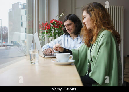 Smiling friends having coffee while using laptop at cafe Stock Photo