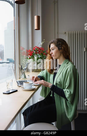 Thoughtful woman using laptop while having coffee at cafe Stock Photo