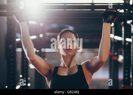 Close-up of young woman doing chin-ups at gym Stock Photo
