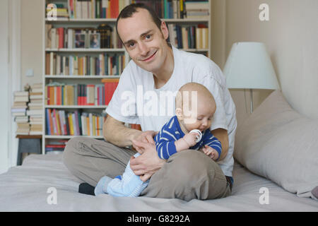 Father and son sitting on bed against bookshelf at home Stock Photo