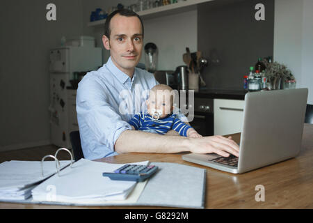 Portrait of father using laptop while carrying son at home Stock Photo