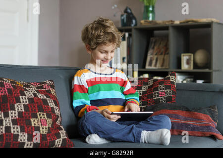 Boy using digital tablet while sitting on sofa at home Stock Photo