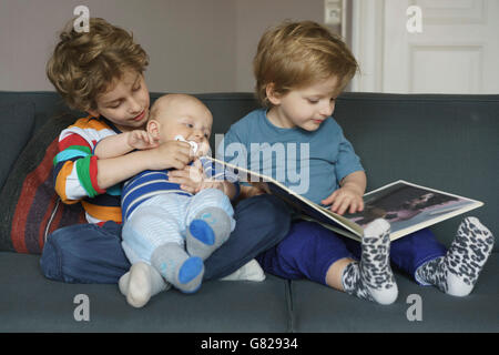 Boy reading book while sitting besides brothers at home Stock Photo