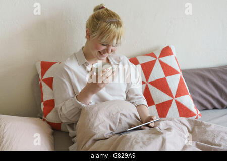 Smiling woman having coffee while using digital tablet on bed at home Stock Photo
