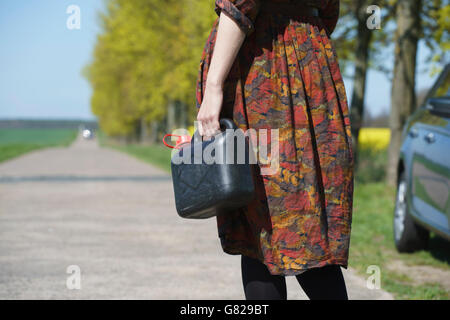 Midsection of young woman holding gas can while standing on road by car Stock Photo