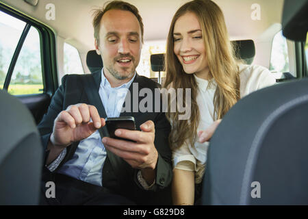 Happy business couple using mobile phone while traveling in car Stock Photo