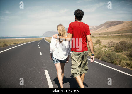 Rear view of couple with arm around walking on road Stock Photo