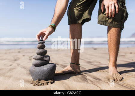 Low section of man balancing stack of stones on beach Stock Photo