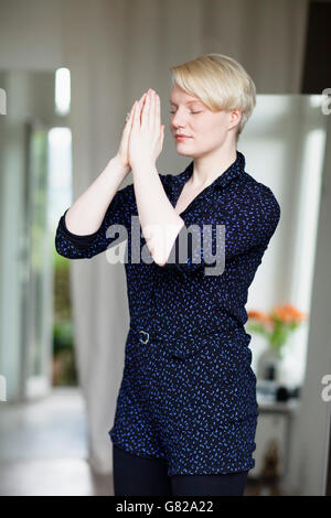 Beautiful mid adult woman in prayer position at home Stock Photo