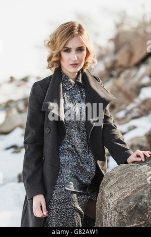 Portrait of beautiful young woman wearing long coat while standing by rock Stock Photo