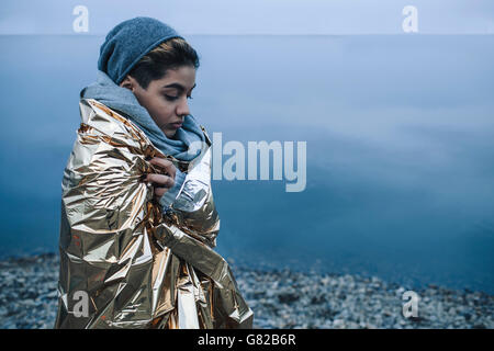 Teenage girl wrapped in golden plastic at lakeshore during winter Stock Photo