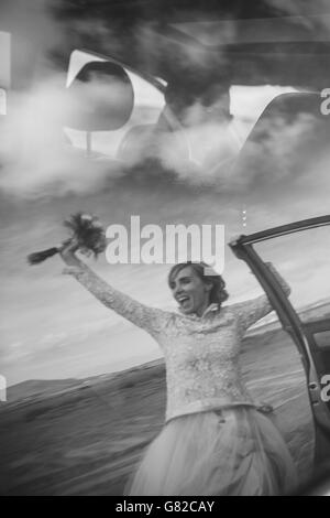 Happy bride holding bouquet and groom driving car Stock Photo