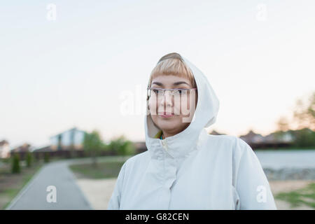 Portrait of smiling woman wearing hood in park against clear sky Stock Photo