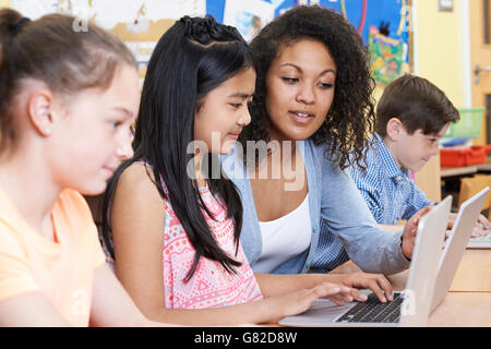 Teacher Helping Group Of Elementary School Children In Computer Class Stock Photo