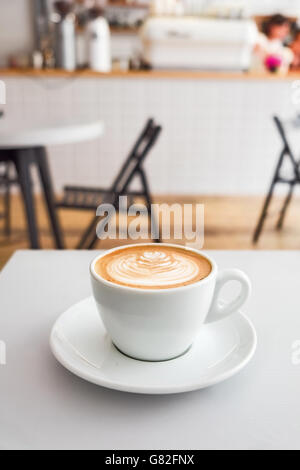 Cappuccino with milk foam art pattern on a white table with a coffee machine on a background. Vertical. Stock Photo