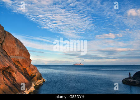 A ferry, Hurtigruten, the Norwegian Coastal Express passing Lofoten Islands, with blue sky and solitry figure Stock Photo