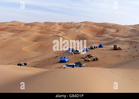 Friends camping in the Middle Eastern desert with off-road vehicles, tents, and kids playing on the dunes Stock Photo