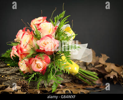 Hand tied red and yellow bicolored rose bouquet with yellow and white ribbon, resting on tree bark with oak leaves. Stock Photo
