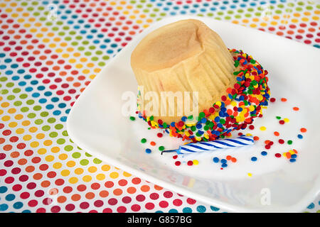 Flipped cupcake with birthday candle and colorful candy sprinkles on white square plate. Stock Photo