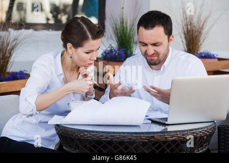 Male and female business colleagues working together on a hard problem at outdoors cafe. They have strained expression on their faces Stock Photo