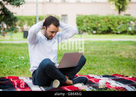 Man is working using laptop at park. Outdoor, guy look challenged and thinking Stock Photo