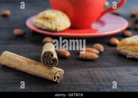 Cinnamon sticks closeup with red teacup, almonds and cookies in the background. Shallow depth of field. Stock Photo