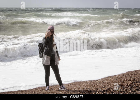 A Spanish visitor takes a selfie as she braves the wind to watch the big waves on the seafront of Brighton, Sussex. Stock Photo