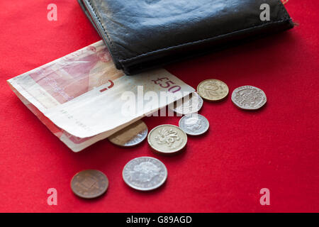 Folded British pounds and coins lying on red background with black wallet beside Stock Photo