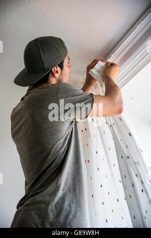 Young handsome man or handyman installing curtains over window at home, doing renovation work Stock Photo