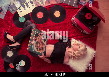 Retro 50's chic: a young blonde woman girl lying down on the floor listening to analogue vinyl music records LPs albums scattered on the floor at home UK Stock Photo