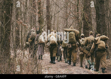 Group Of Unidentified Re-enactors Dressed As World War II Russian Soviet Soldiers In Camouflage Walks Through Forest. Stock Photo