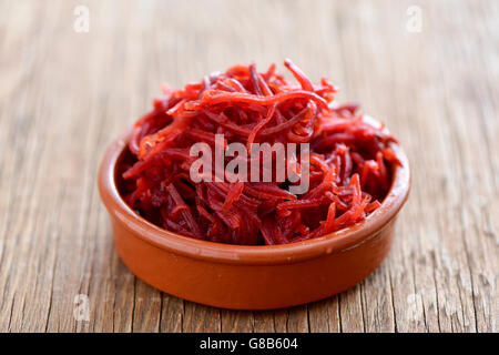 an earthenware bowl with a pile of grated beetroot on a rustic wooden surface Stock Photo